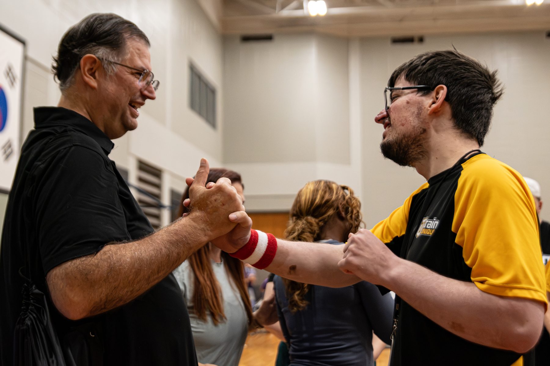 A man and an athlete in a Train Unique shirt clasp hands and smile at each other