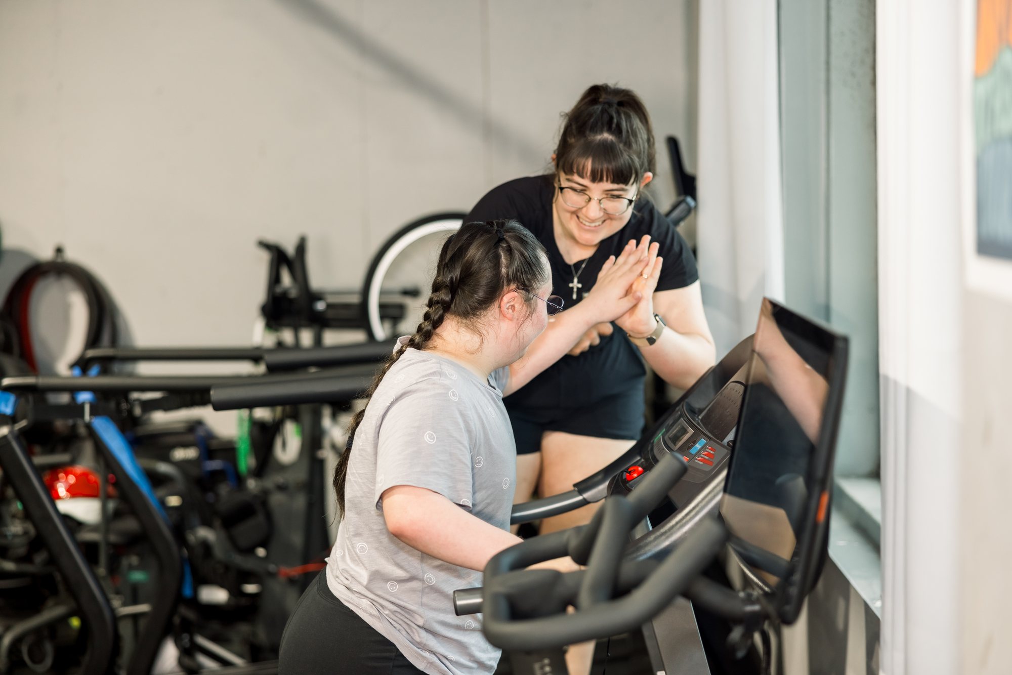 Coach Emily and an athlete on an exercise bike high-five, both smiling