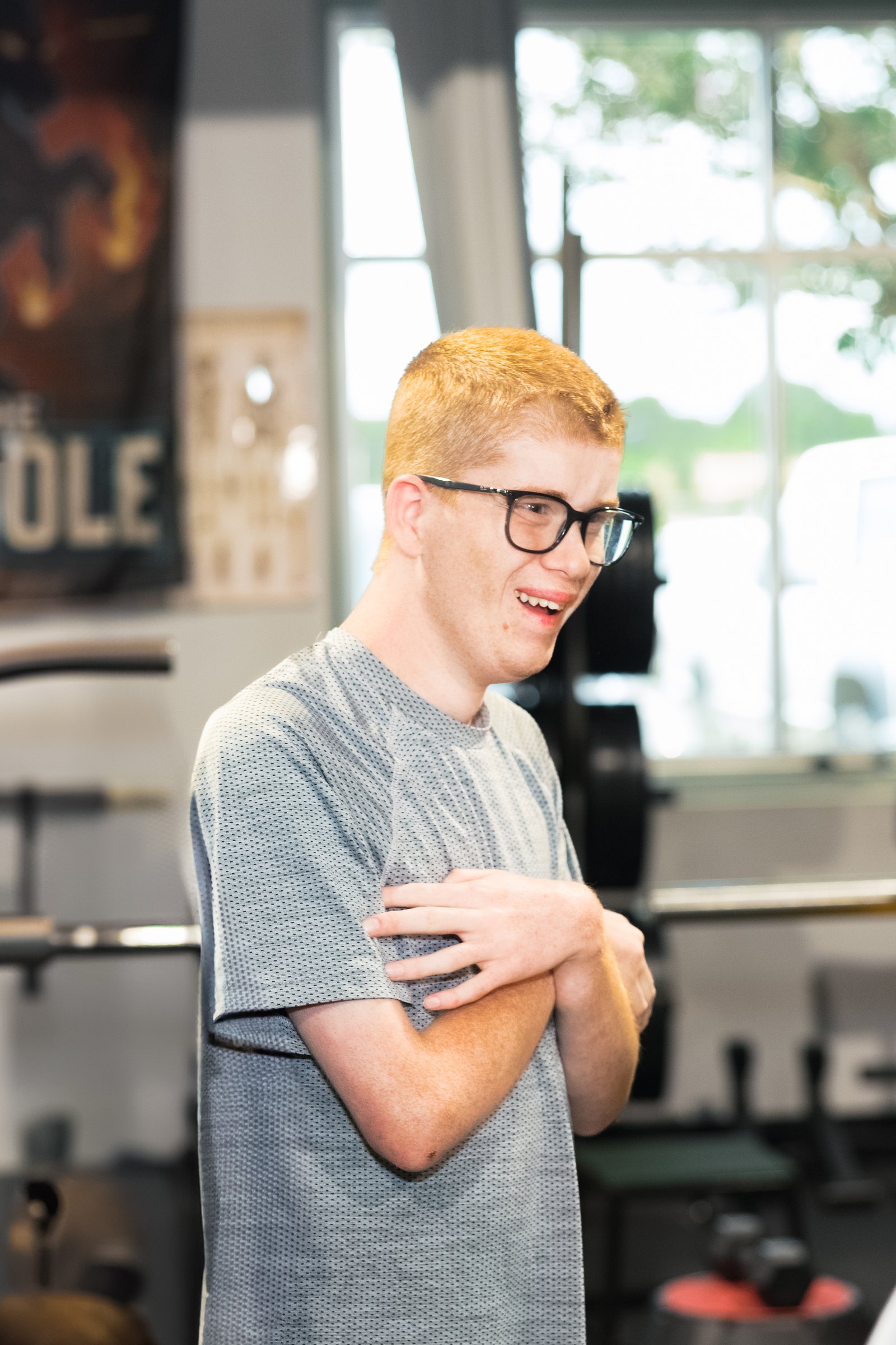An athlete in glasses folds his arms and smiles on the gym floor