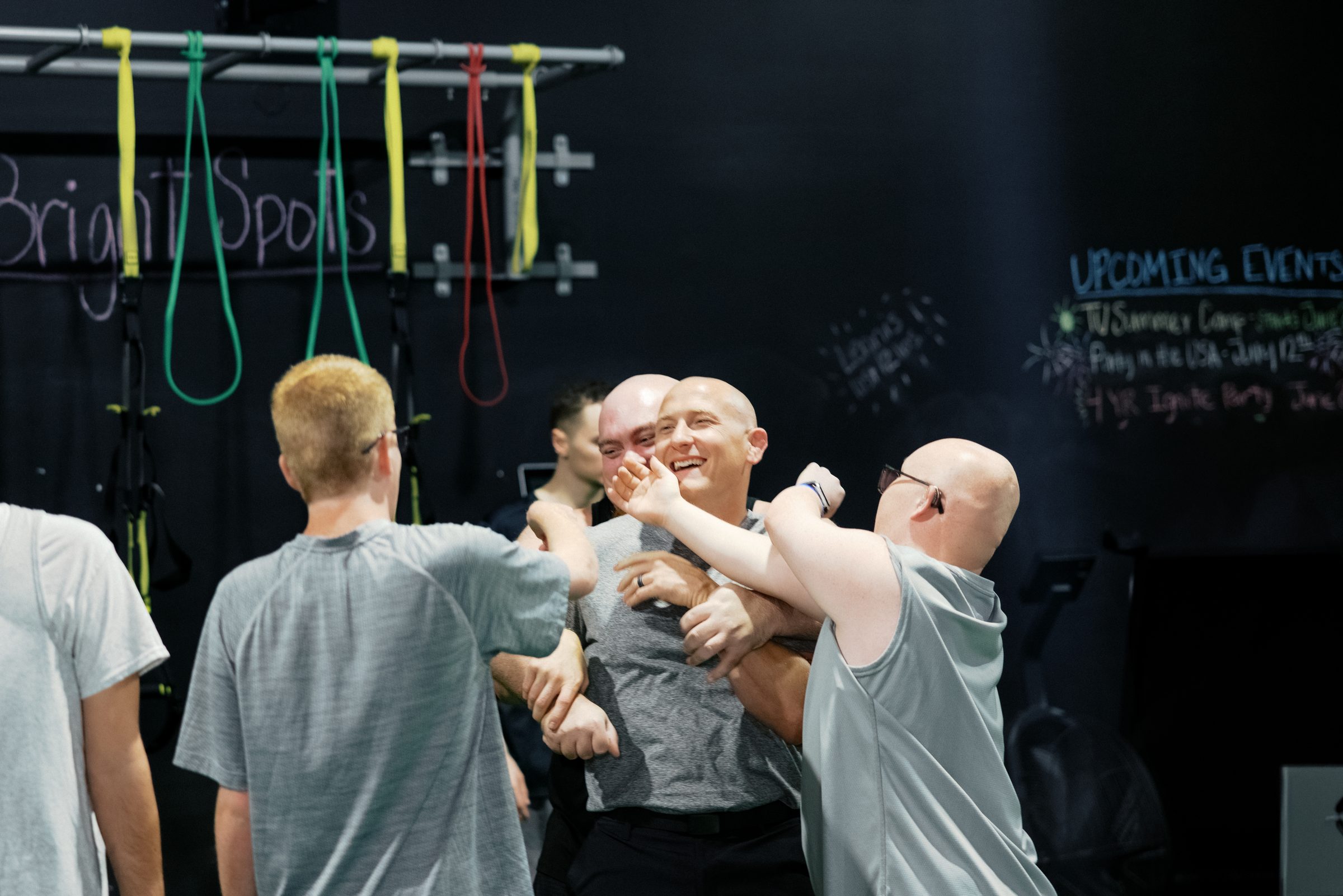 A coach laughs as athletes crowd in around him, one with an arm around his shoulders