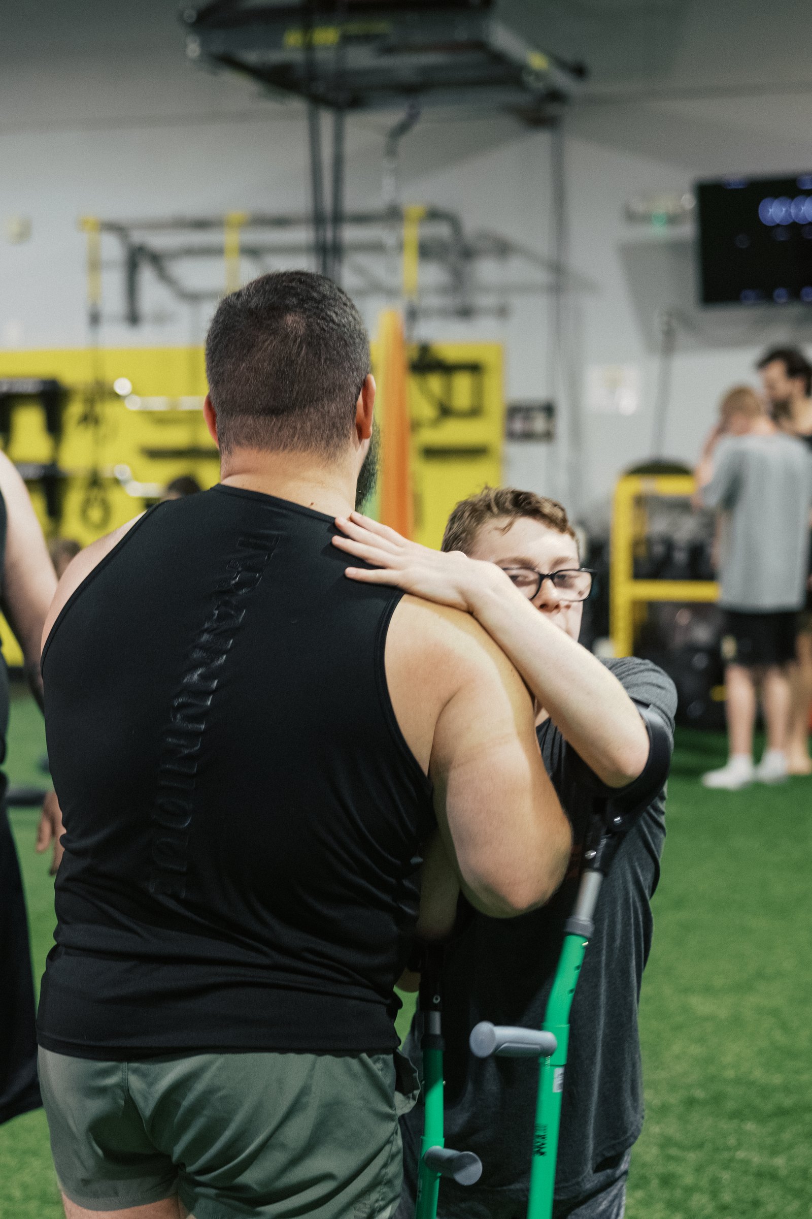 An athlete with a forearm crutch wraps an arm around his coach's shoulders in a hug
